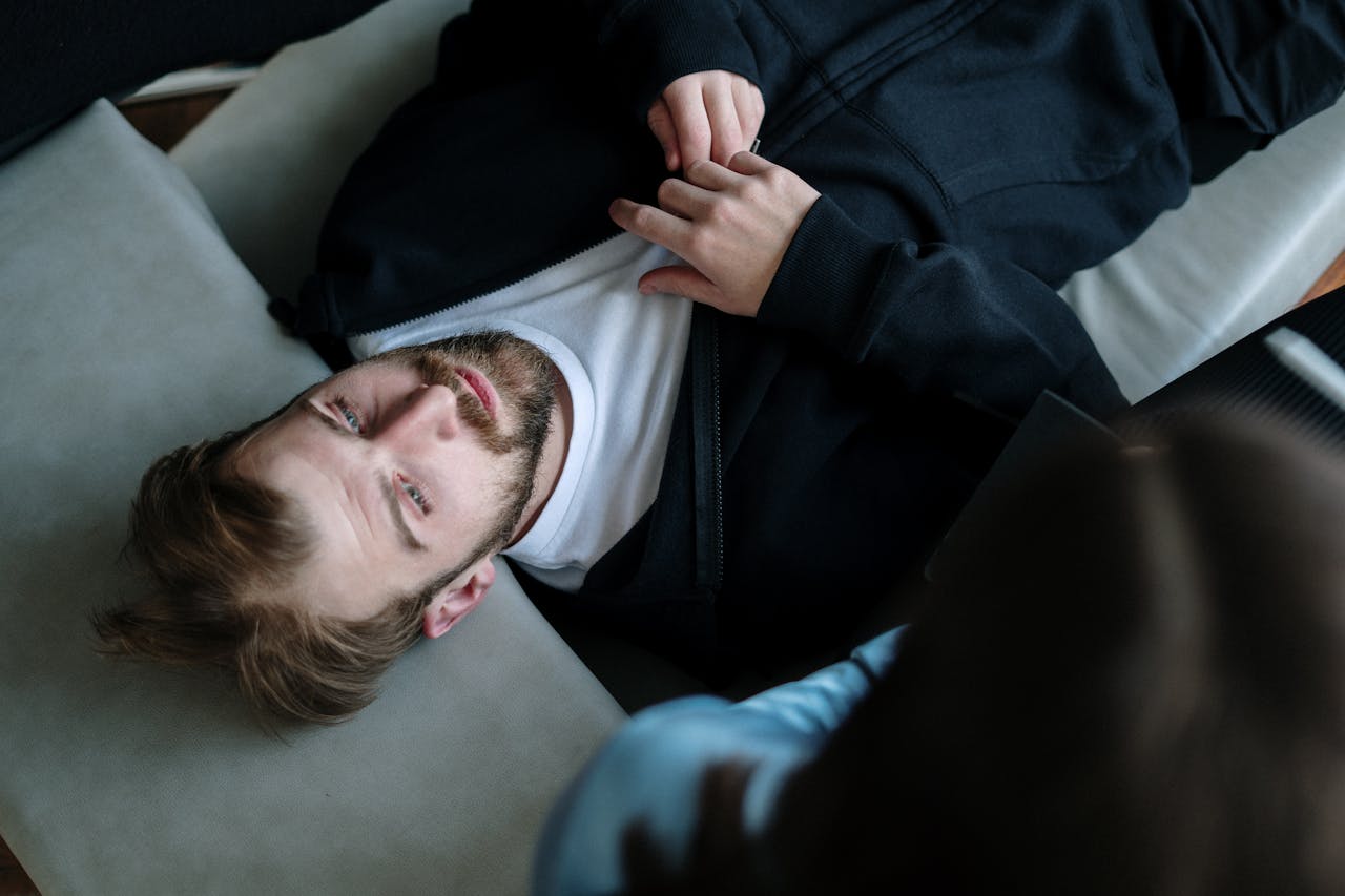 Services A bearded man lying down during a therapy session indoors, expressing emotions.