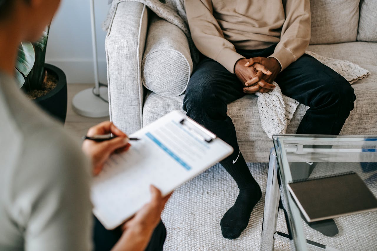 Services Therapist takes notes as client sits on a sofa during a psychotherapy session.